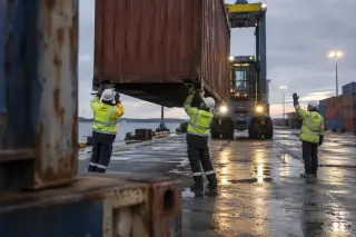 Sur le quai d’un terminal à conteneurs, des dockers retirent les verrous d’un conteneur suspendu au portique