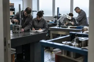 Dans la salle de métrologie d’un centre de formation, des adultes mesurent des pièces usinées sur un marbre en granit